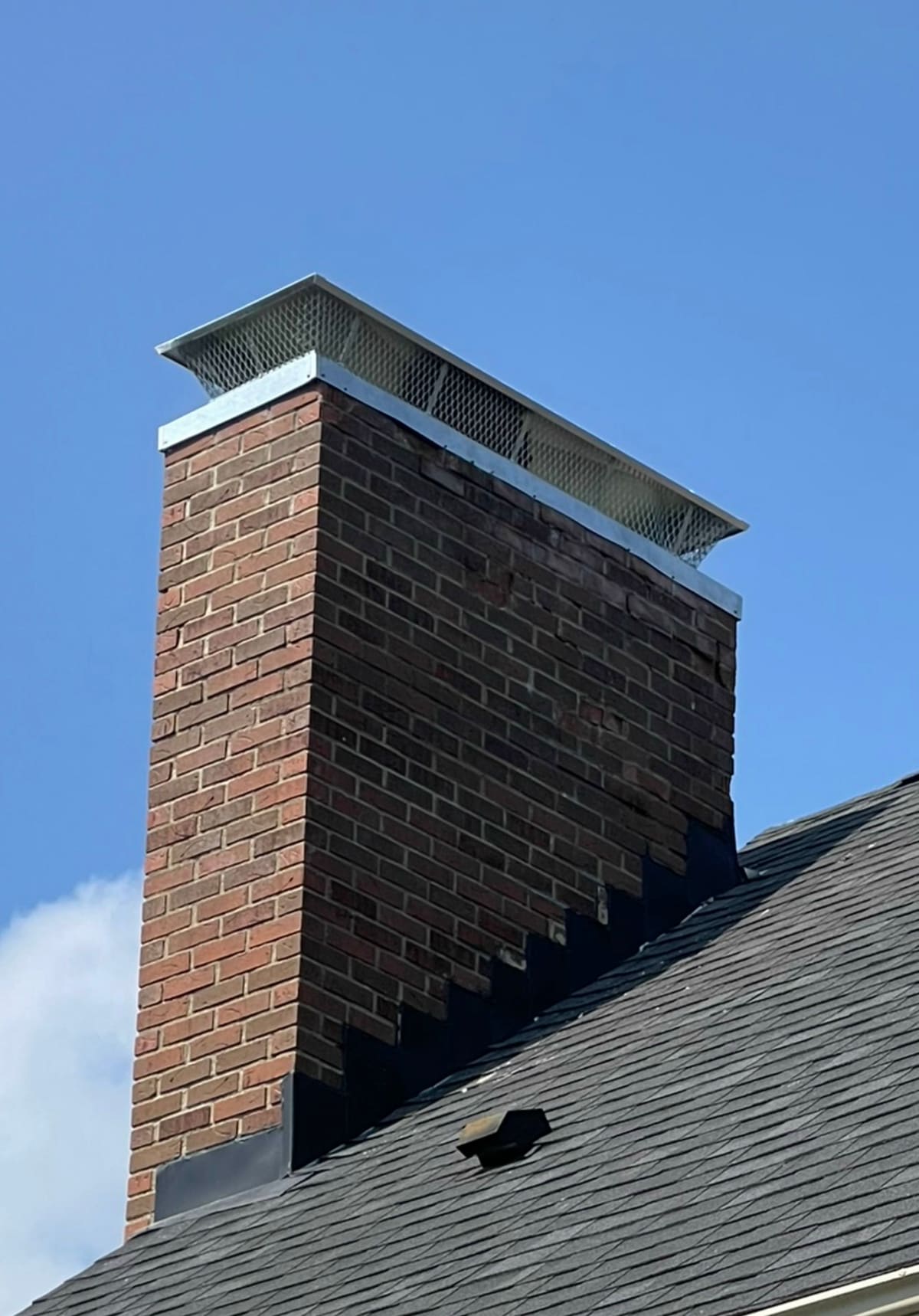 Tall brick chimney with a new metal cap and fresh flashing against a clear sky