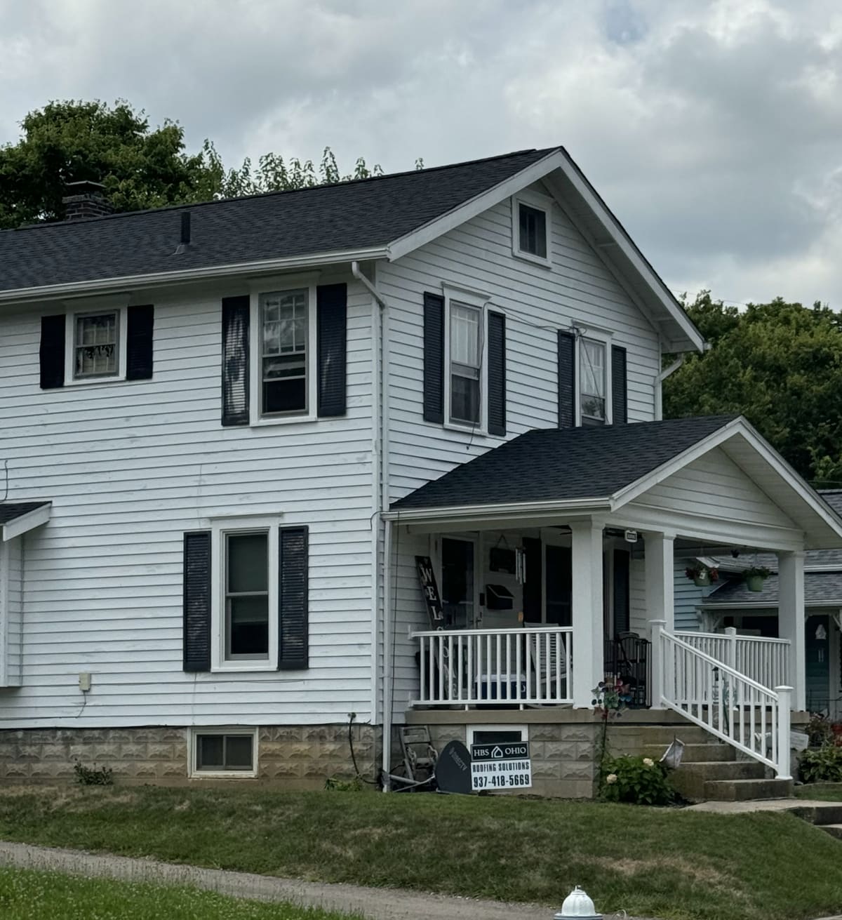 White two-story farmhouse with black shutters and a new dark roof over the porch