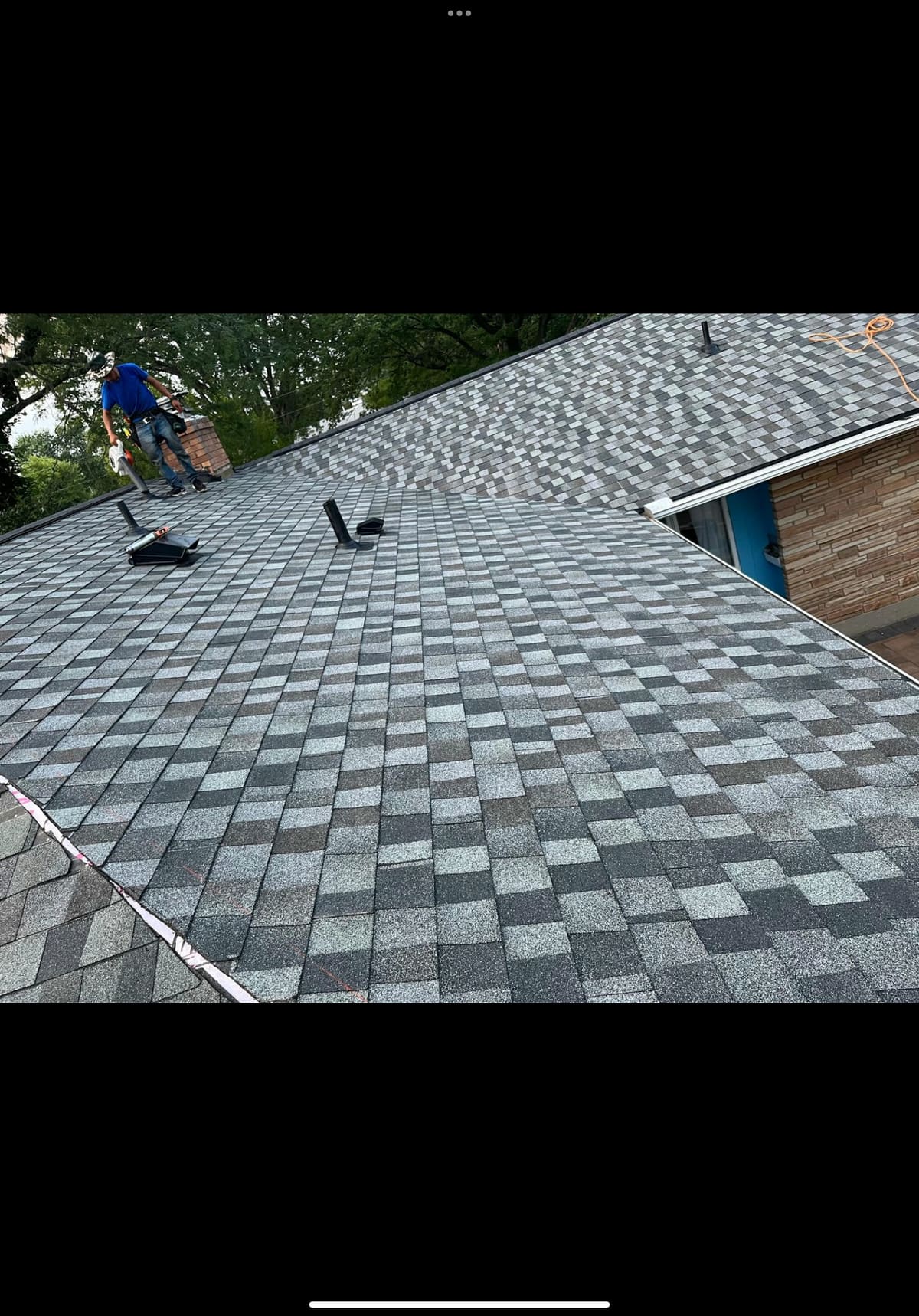 Roofer working up a gray shingle field with fresh sheathing exposed at the rake edge