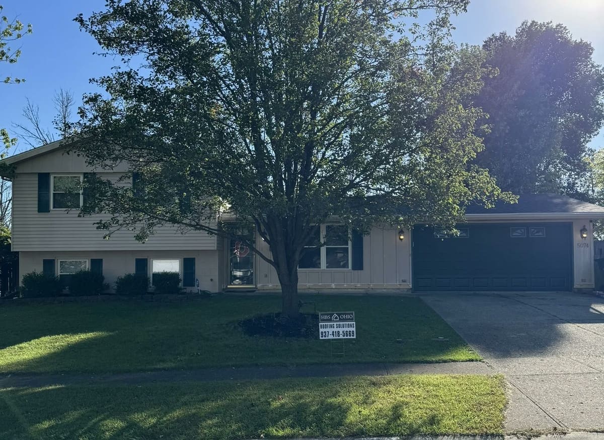 Two-story home under heavy tree cover, the kind of shade that keeps a roof damp