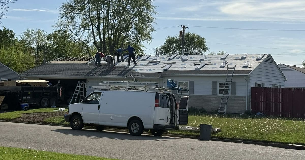 Crew working along a ranch roofline with ladders up and the work van parked at the curb