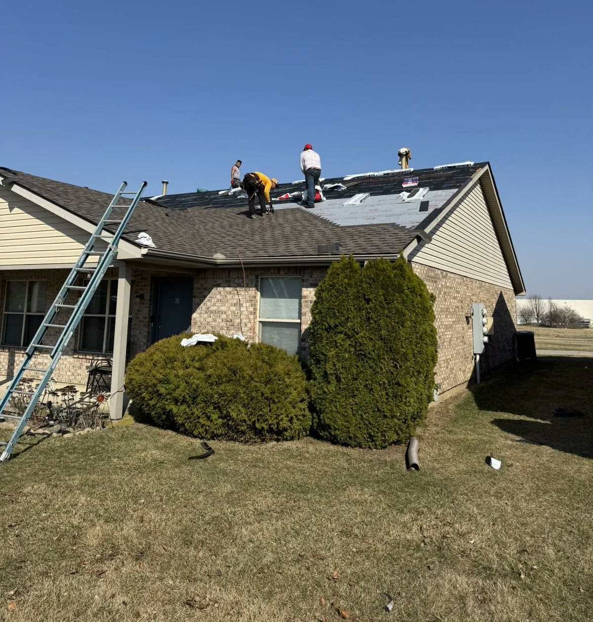 Three roofers on the roof of a two-story brick home with an extension ladder in place