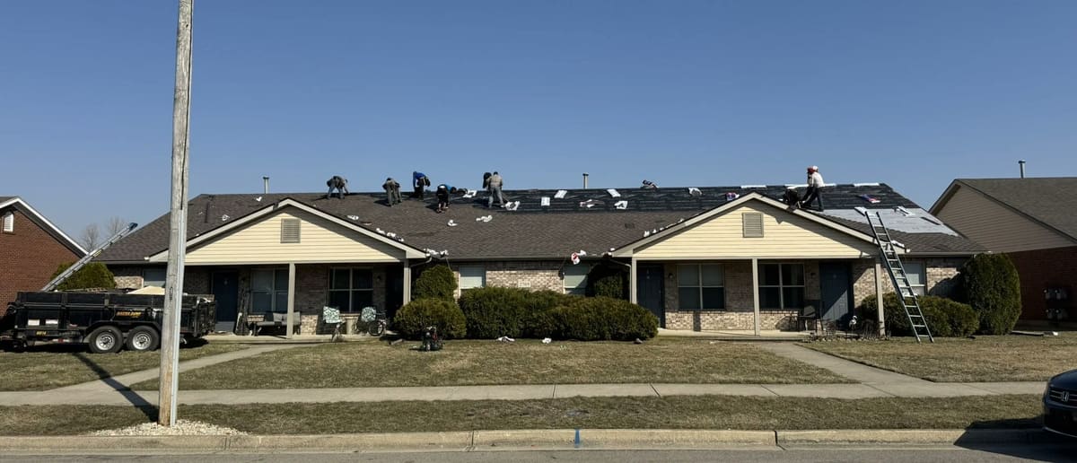 Roofing crew spread across the long roof of a multi-unit building, mid tear-off