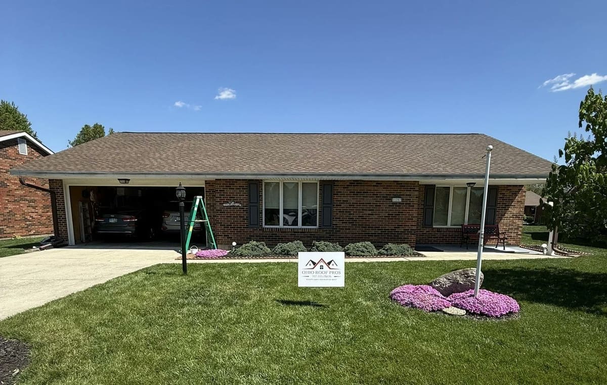 Brick ranch with a completed roof and an Ohio Roof Pros yard sign by the flower bed